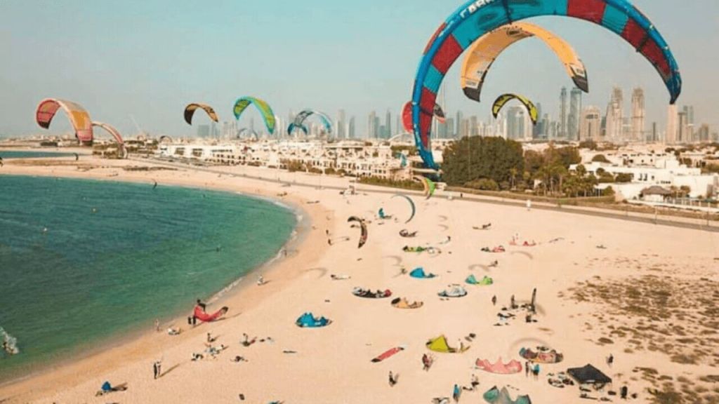 Aerial view of Kite Beach Dubai showing kitesurfers, white sand, food trucks, and Burj Al Arab hotel during sunset